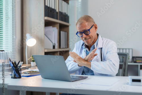 Foto Doctor gesturing stop with crossed arms during a video call on his laptop in med