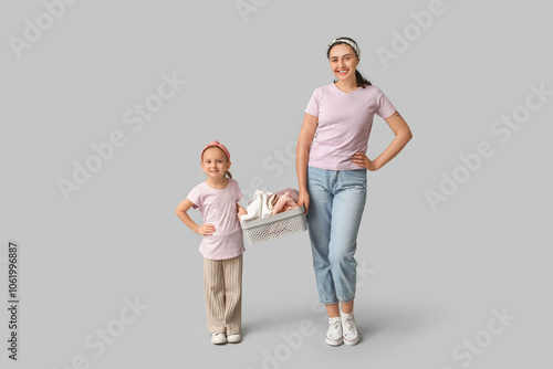 Happy mother and her daughter with clean towels in basin on grey background