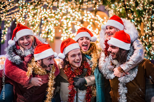 Happy group of friends wearing Santa Claus hat and celebrating Christmas night together - Young people having fun during winter holidays - Teenagers celebrating New Year's Eve in front of tree