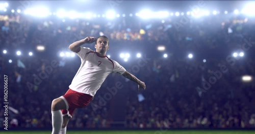 Football player, wearing red and white uniform, kicks the ball in a jump, in slow motion on the professional football stadium with animated crowd.
