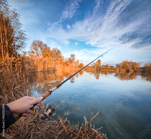 Fishing with spinning for a predator on a picturesque autumn lake. A hand with a fishing rod