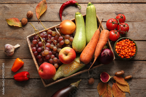 Fototapeta Naklejka Na Ścianę i Meble -  Wicker box with different fresh vegetables, fruits and autumn leaves on wooden background. Harvest festival