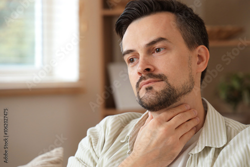 Handsome man self-examining thyroid gland at home, closeup