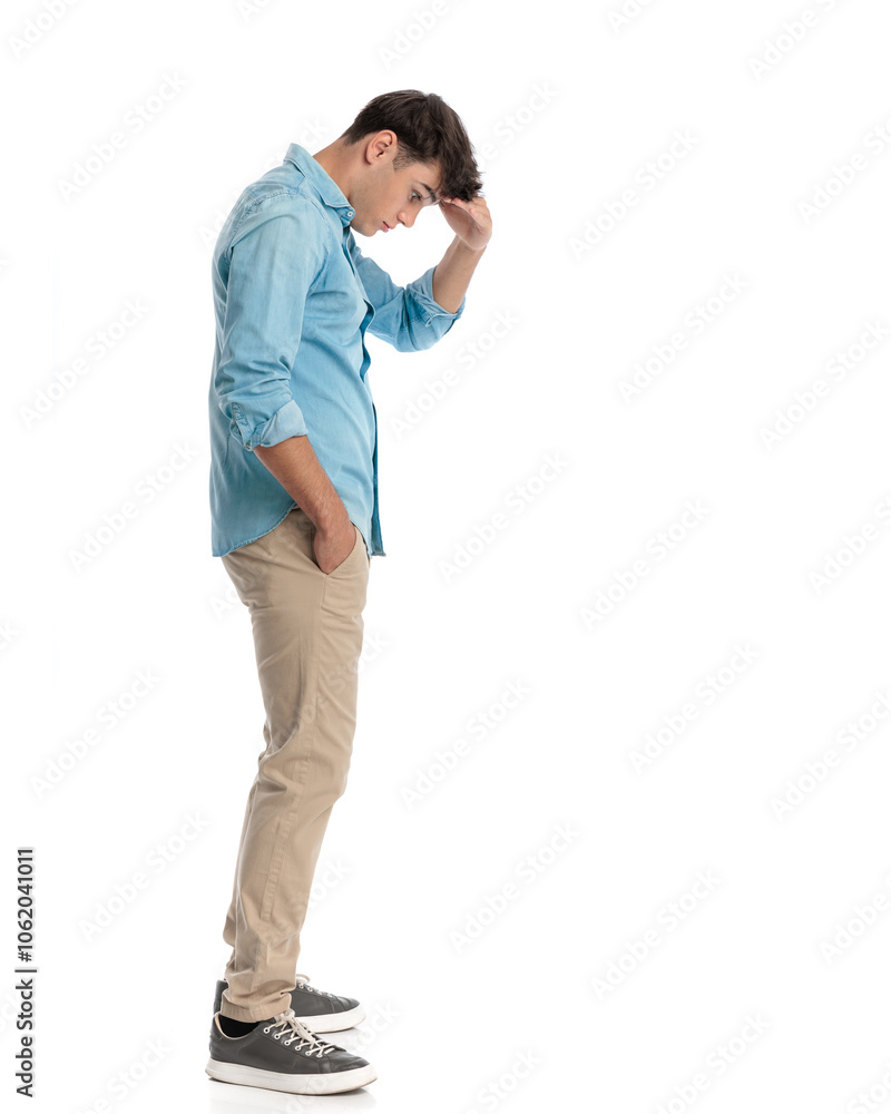 handsome student focused on the floor, holding hand to forehead handsome student focused on the floor, holding hand to forehead