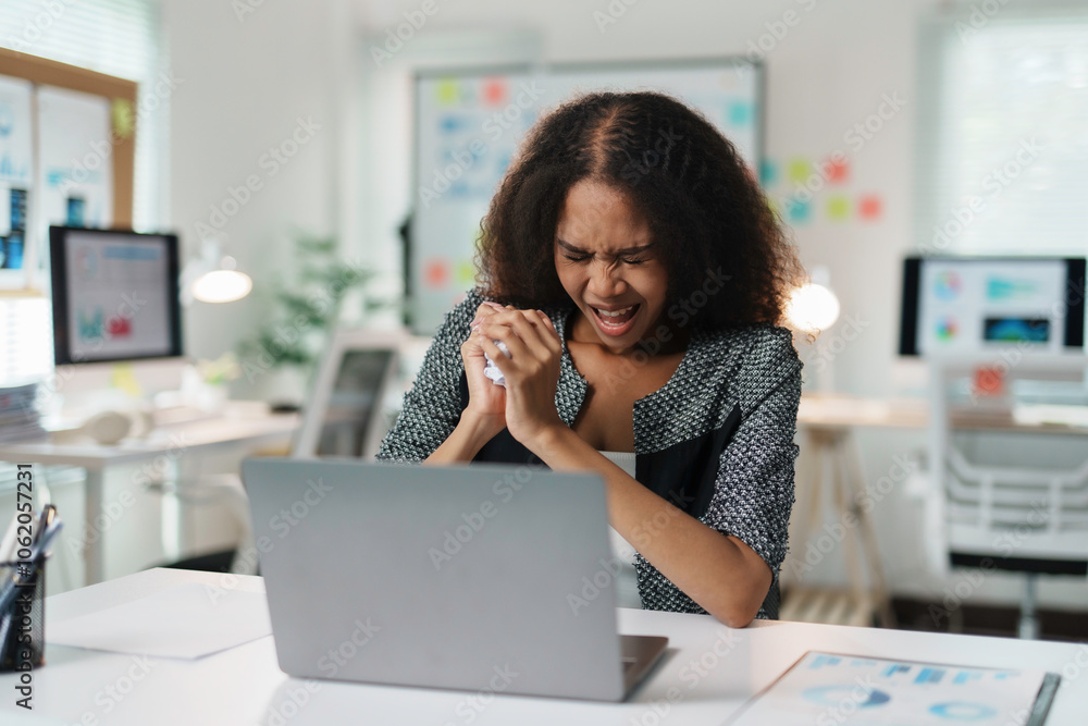 Frustrated office worker crumpling paper while working on laptop, experiencing work stress and burnout in modern office Frustrated office worker crumpling paper while working on laptop, experiencing work stress and burnout in modern office
