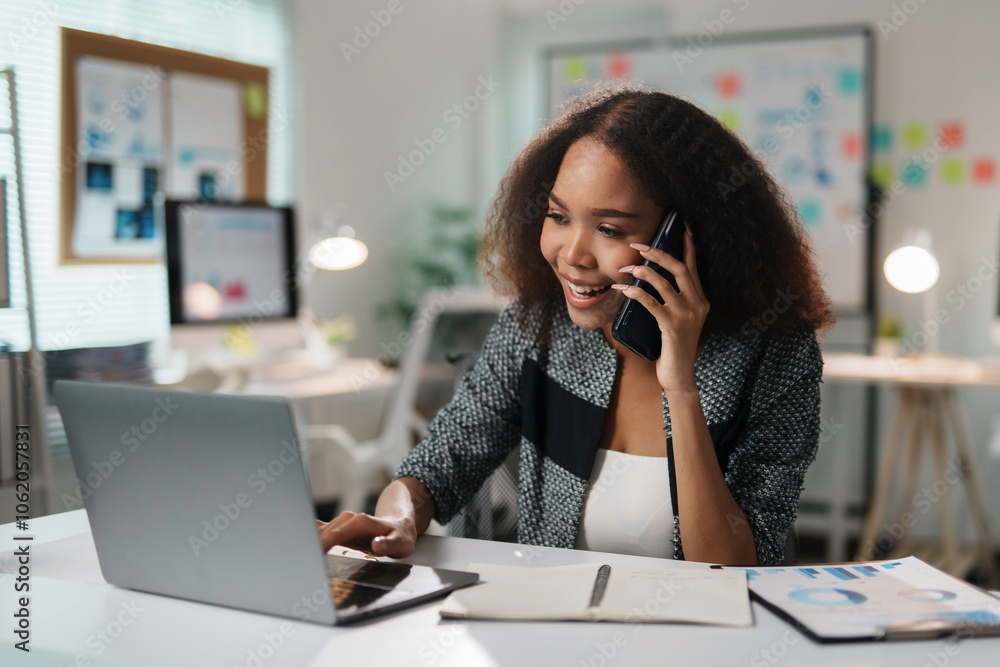 Smiling businesswoman multitasking, talking on mobile phone and working on laptop, enjoying productive workday in modern office Smiling businesswoman multitasking, talking on mobile phone and working on laptop, enjoying productive workday in modern office