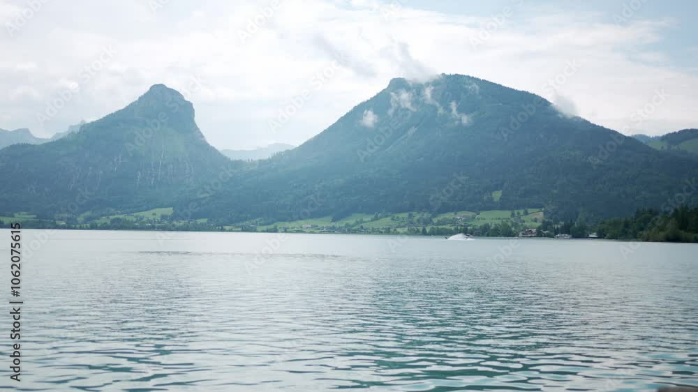 Summer scene of people enjoying water ski on the Wolfgangsee Lake with the gorgeous green mountains in the background. Blue Sky and light rain clouds. Summer scene of people enjoying water ski on the Wolfgangsee Lake with the gorgeous green mountains in the background. Blue Sky and light rain clouds.