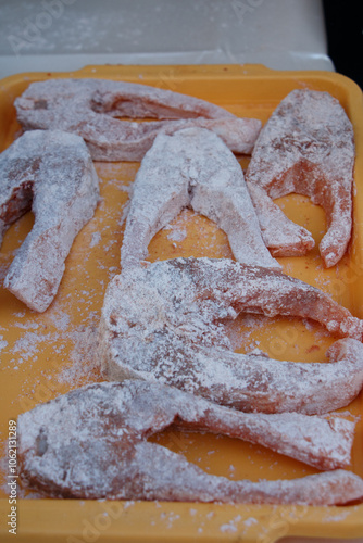 Several raw fish slices coated in flour are arranged on a yellow tray, ready for cooking.  photo