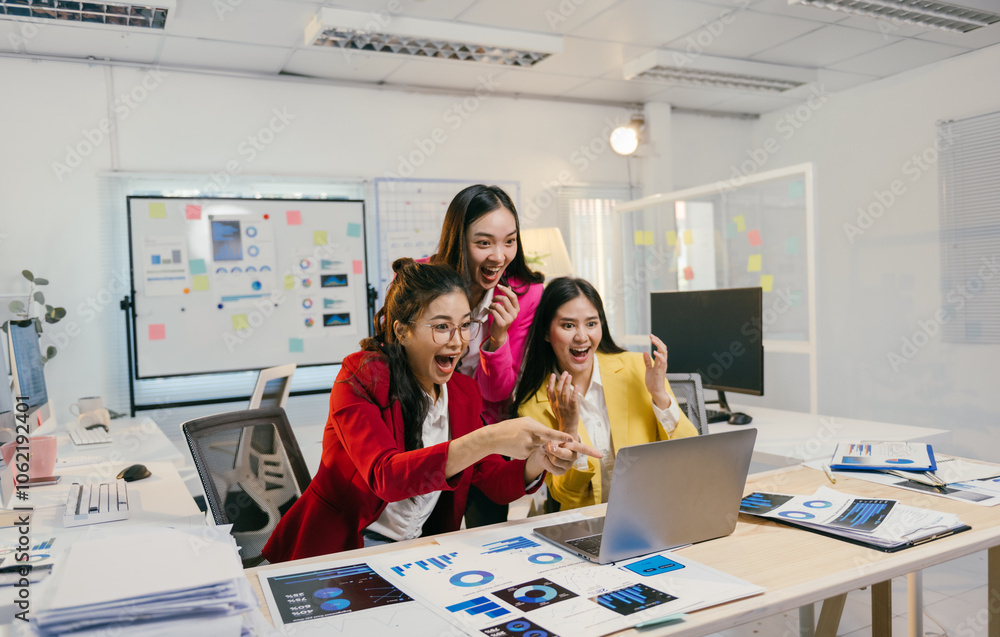 Three young businesswomen are excitedly pointing at a laptop screen, celebrating a positive outcome based on the charts and data they are analyzing in a modern office environment Three young businesswomen are excitedly pointing at a laptop screen, celebrating a positive outcome based on the charts and data they are analyzing in a modern office environment