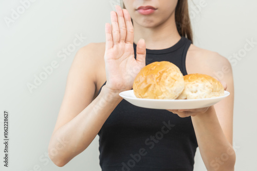 Gluten allergy, asian young woman hand push out, refusing to eat white bread loaf on plate in breakfast food meal at home, girl having a stomach ache. Gluten intolerant and Gluten free diet concept. photo