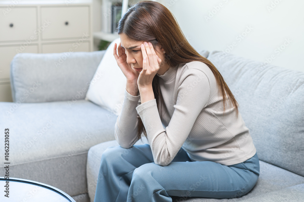Depressed anxiety asian young woman frustrated hand on head, touching her temples, suffering stressed, sick, tired, crisis on sofa from headache, migraine pain tension problem health care concept. Depressed anxiety asian young woman frustrated hand on head, touching her temples, suffering stressed, sick, tired, crisis on sofa from headache, migraine pain tension problem health care concept.