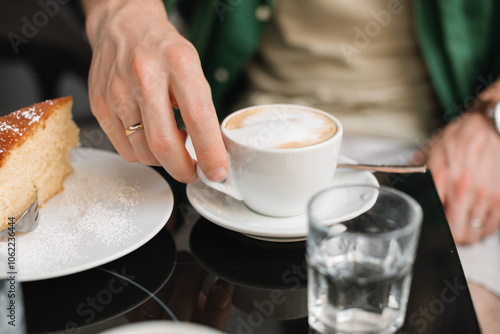 Man sitting at an outdoor cafe drinking a cappuccino and eating a slice of lemon cake