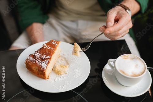 Man sitting at an outdoor cafe drinking a cappuccino and eating a slice of cake