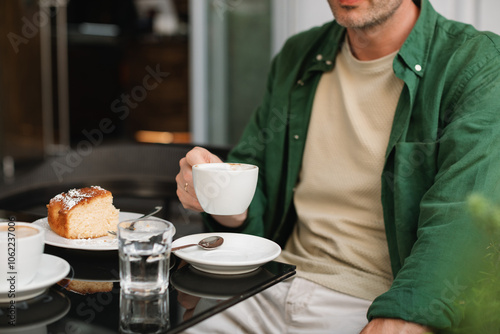 Man sitting at an outdoor cafe drinking a cappuccino and eating a slice of cake