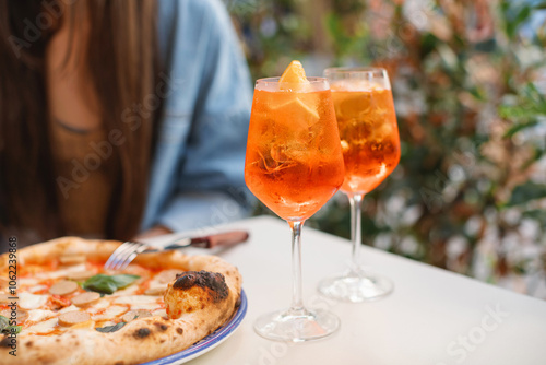 Close-up of a woman enjoying a traditional Italian sausage pizza and orange spritz cocktail