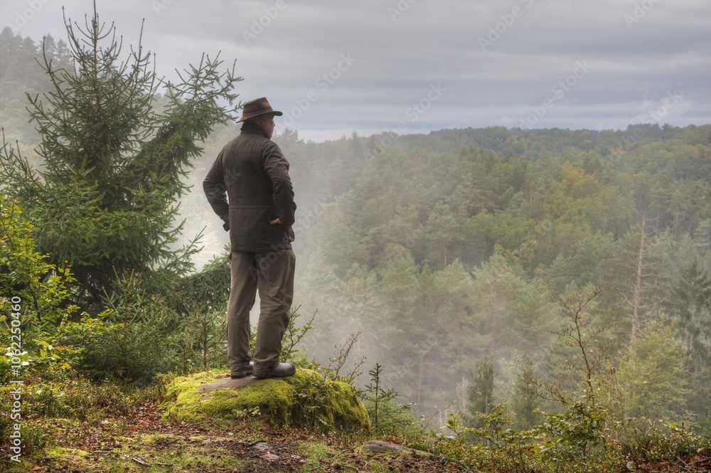 In September, a solitary hiker stands early in the morning on a rocky outcrop, gazing down at the mysterious, mist-covered Palatinate Forest below him. In September, a solitary hiker stands early in the morning on a rocky outcrop, gazing down at the mysterious, mist-covered Palatinate Forest below him.