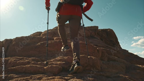 Active hiker or tourist with backpack and hiking poles climbs uphill at rocky terrain and stops on the top in winner pose with open arms photo