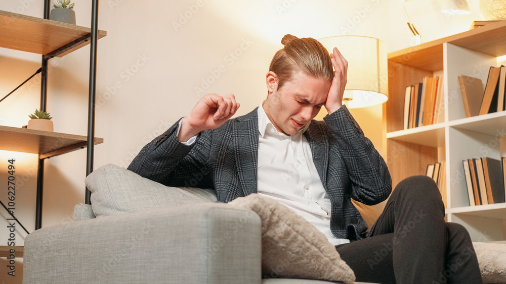 Fototapeta premium Headache pain. Health story. Business man suffering migraine on sofa in modern suit with lighted lamp in modern interior.