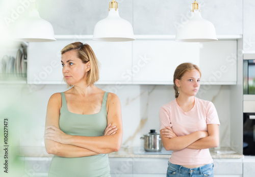 After conflict unpleasant conversation, mother and teenage daughter do not talk to each other. Woman and girl crossed arms and are standing apart photo