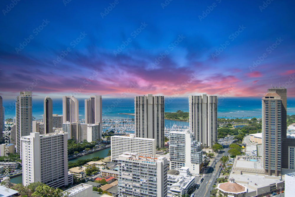 Fototapeta premium aerial shot of the Ala Wai Canal with skyscrapers, hotels and condos, lush green trees and cars driving on the street, boats and yachts in the harbor in Honolulu Hawaii USA