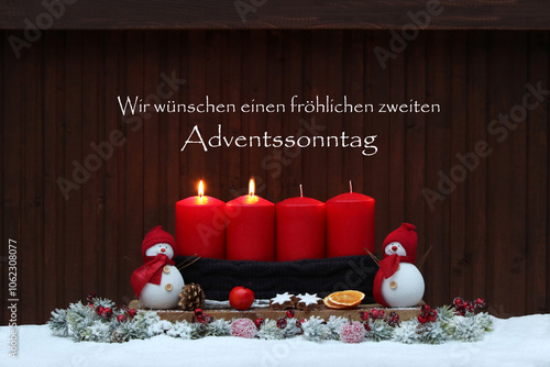 Zweiter Advent: Adventsdekoration mit vier roten Adventskerzen, Schneemann, Weihnachtsschmuck im Schnee und dem Text wir wünschen einen fröhlichen zweiten Adventssonntag. photo