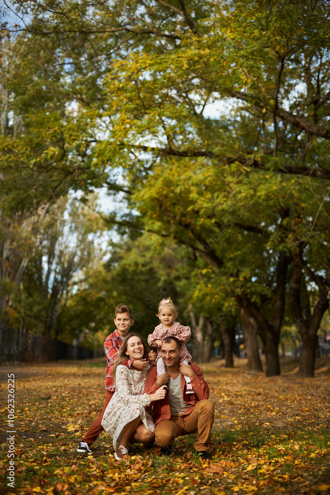 Happy family walking on green grass strewn with fallen leaves in Park in autumn. Parents, two children are walking in park hug and laugh. Family, child, walk through Autumn Park. Happy family walking on green grass strewn with fallen leaves in Park in autumn. Parents, two children are walking in park hug and laugh. Family, child, walk through Autumn Park.