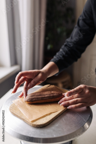 Woman pastry chef serving chocolate eclair on baking sheet