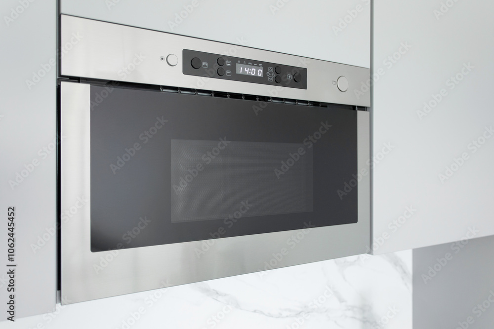 Fototapeta premium Modern built-in electric microwave oven in light grey kitchen interior. Technology and cooking appliance