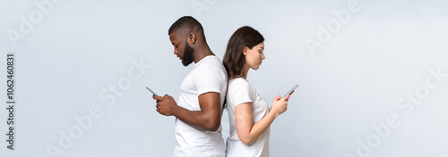 Gadget addiction and relationship problems. Interracial couple standing back to back with smartphones, ignoring each other after quarrel photo