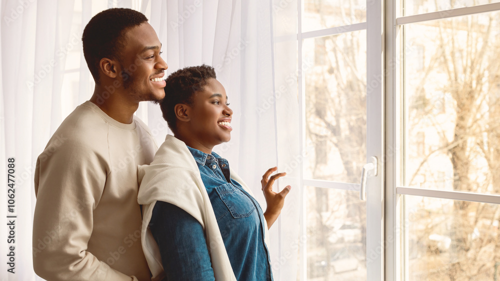 Enjoying Morning Together. Happy casual African American couple standing and looking through the glass window indoors, positive bearded man embracing curvy lady from back, banner, free space Enjoying Morning Together. Happy casual African American couple standing and looking through the glass window indoors, positive bearded man embracing curvy lady from back, banner, free space