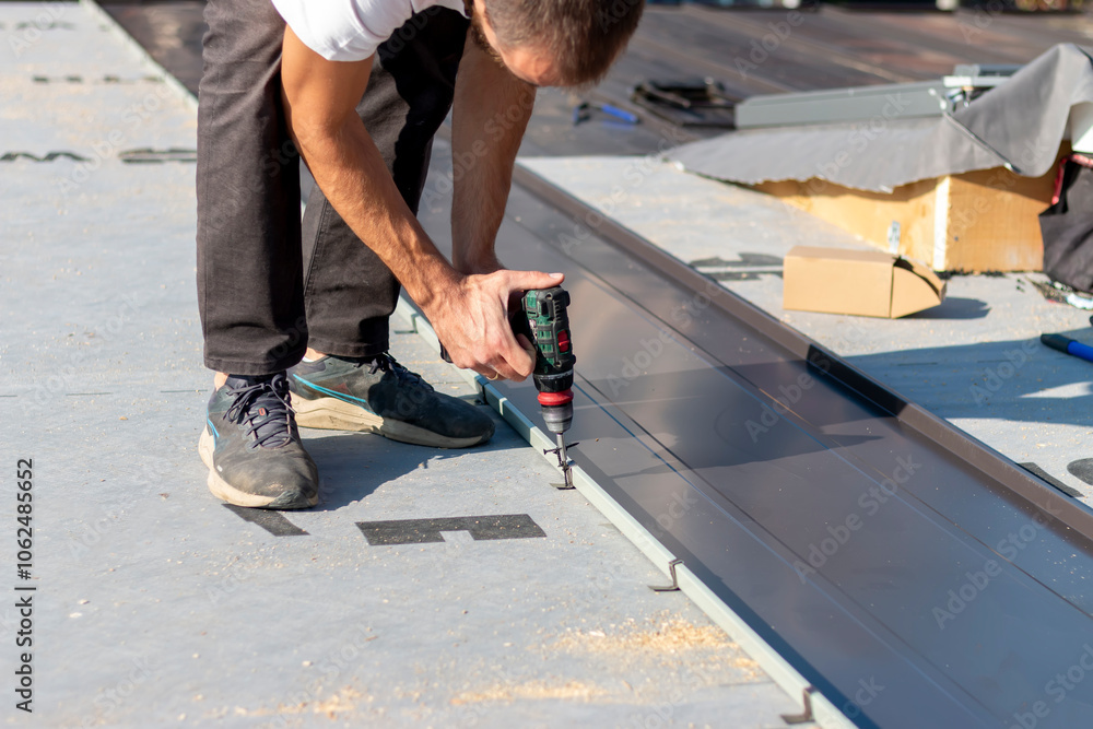 Roofer assembles sheet metal on the roof. Tinsmith worker using cordless drill screws to install new metal sheet roof Roofer assembles sheet metal on the roof. Tinsmith worker using cordless drill screws to install new metal sheet roof