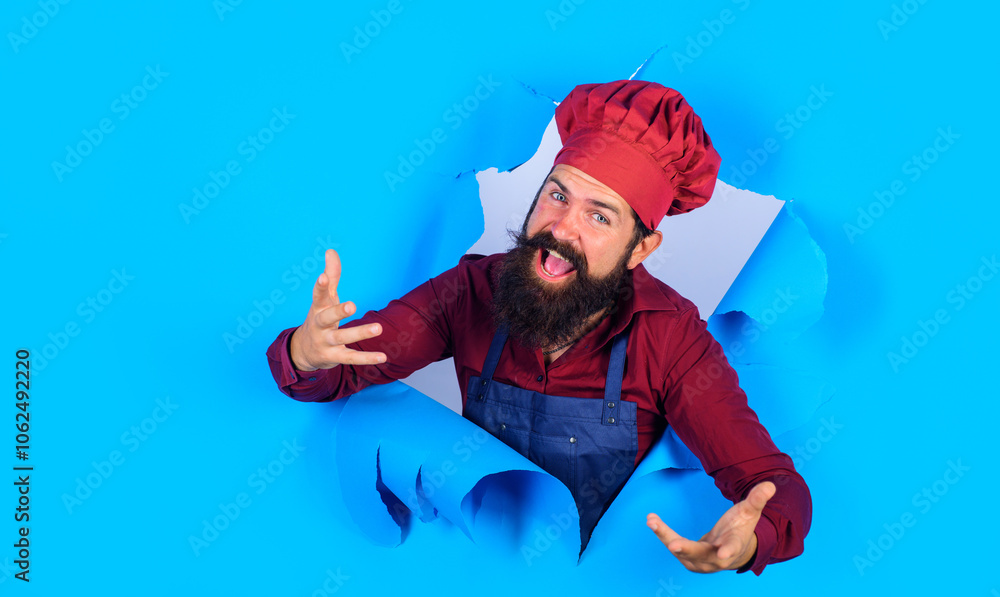 Happy bearded man in chef uniform looking through hole in paper. Professional chef man. Cooking profession and culinary. Smiling male cook in chef hat, uniform and apron. Copy space for advertising. Happy bearded man in chef uniform looking through hole in paper. Professional chef man. Cooking profession and culinary. Smiling male cook in chef hat, uniform and apron. Copy space for advertising.