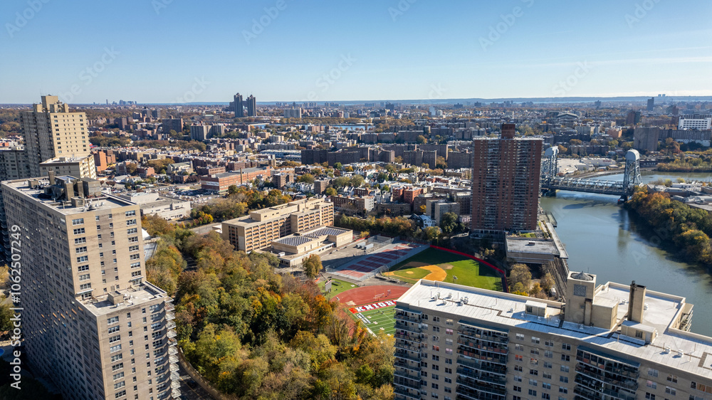 Fototapeta premium This location in the Bronx offers stunning views of lush greenery, a picturesque lake, and urban structures. Framed by the river, it showcases iconic bridges and the New York City skyline in the dista