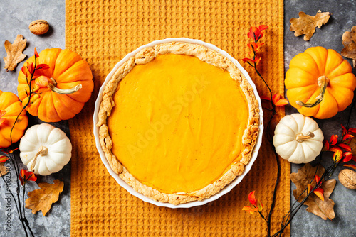 Delicious homemade pumpkin pie on orange towel surrounded by autumn leaves and pumpkins. Thanksgiving, fall concept. photo