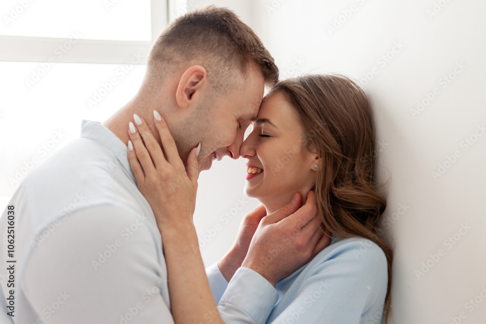 young couple in love stands close, holds the neck and looks into the eyes before kissing, the man passionately kisses the woman at home and smiles, close-up young couple in love stands close, holds the neck and looks into the eyes before kissing, the man passionately kisses the woman at home and smiles, close-up