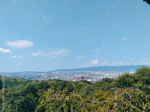 This panoramic cityscape showcases a sprawling urban area with distant hills and a clear blue sky, offering a serene glimpse of urban life amidst nature.