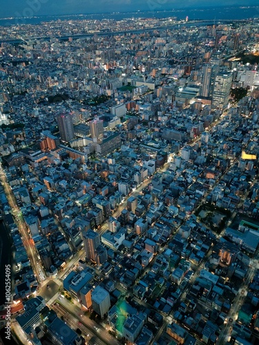 An aerial shot capturing the vibrant cityscape during blue hour, highlighting its dense architecture, illuminated streets, and the bustling urban life below.