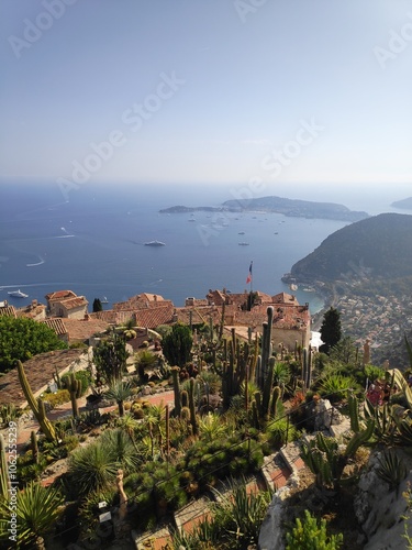 An exquisite view over the Mediterranean coast featuring lush gardens with various cacti, alongside distant islands and the wide expanse of the sea in the background.