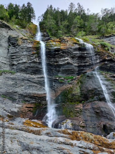 A stunning waterfall cascades gracefully down a rugged rocky mountainside, surrounded by lush greenery, capturing the majesty and power of nature in this serene scene.