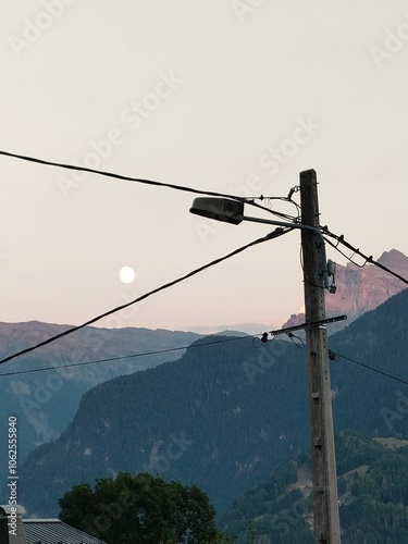 A tranquil mountain landscape bathed in the gentle light of early morning, featuring an enchanting view of the moon rising over towering ridges and a calm atmosphere.