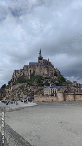 A stunning view of Mont Saint-Michel rising dramatically against a backdrop of clouds, showcasing its grandeur and architectural magnificence on a rocky island.