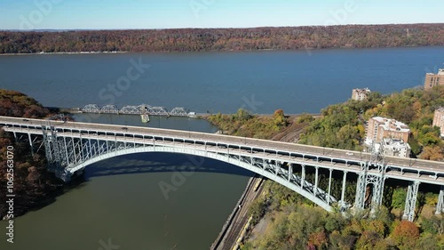 This aerial view captures the Henry Hudson Bridge gracefully arching over the river, connecting the Bronx to Manhattan. Surrounded by lush foliage and scenic water views, the bridge stands as a striki