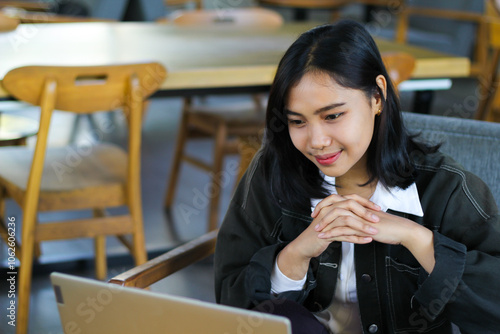 pretty asian woman using laptop in cafe doing virtual online meeting with client and watching course webinar with smile face