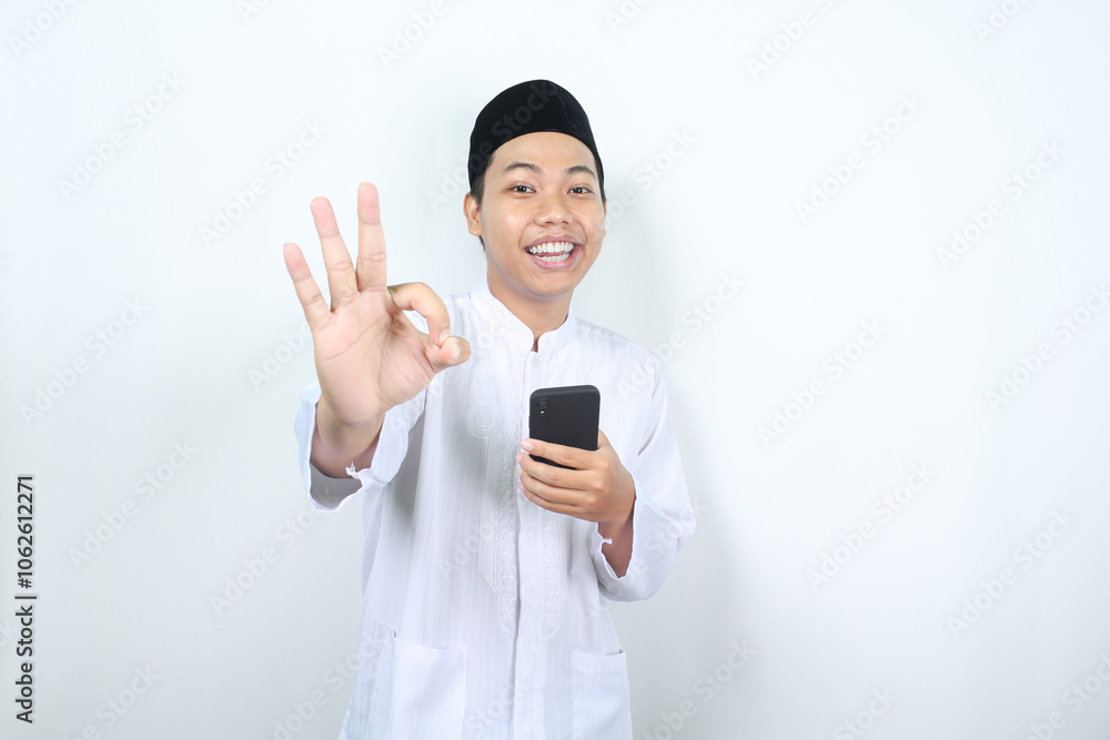 smiling asian muslim man showing okay signs with holding mobile phone isolated smiling asian muslim man showing okay signs with holding mobile phone isolated