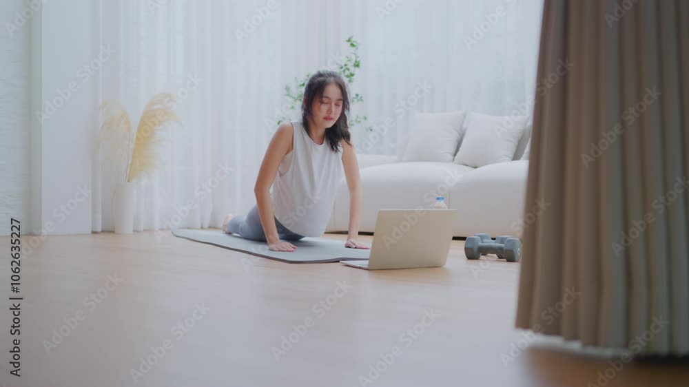 Young Asian woman stretching yoga workout on exercise mat while online training class with computer laptop in living room Young Asian woman stretching yoga workout on exercise mat while online training class with computer laptop in living room