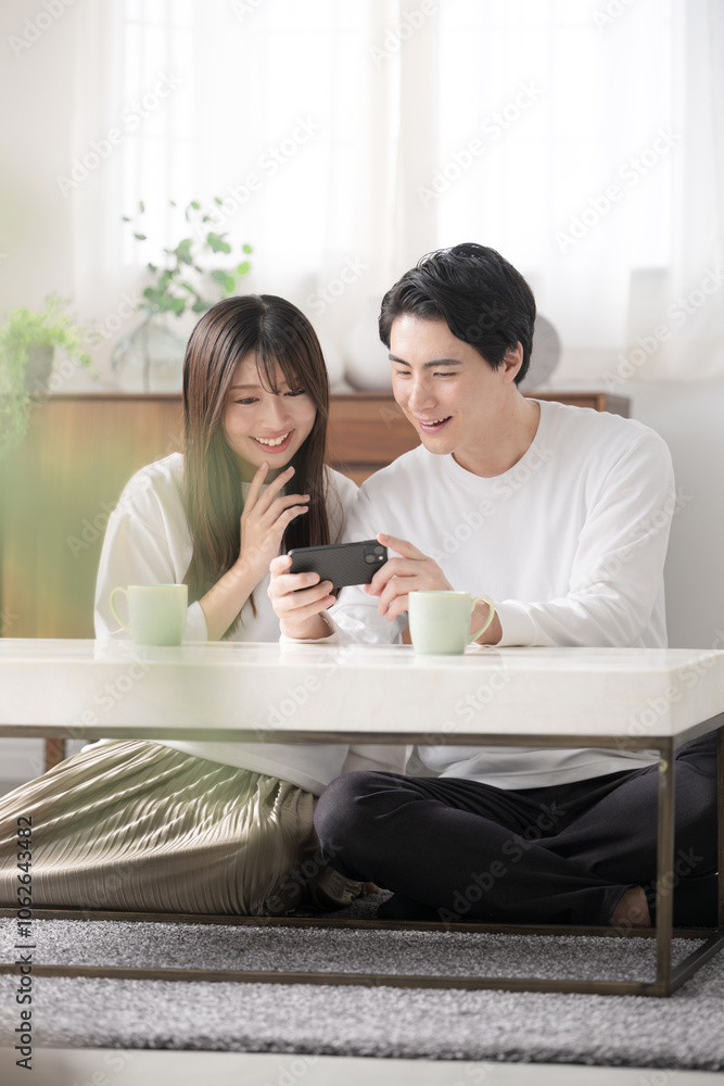 リビングでスマホで動画などを見る男女の若いカップルや夫婦 リビングでスマホで動画などを見る男女の若いカップルや夫婦