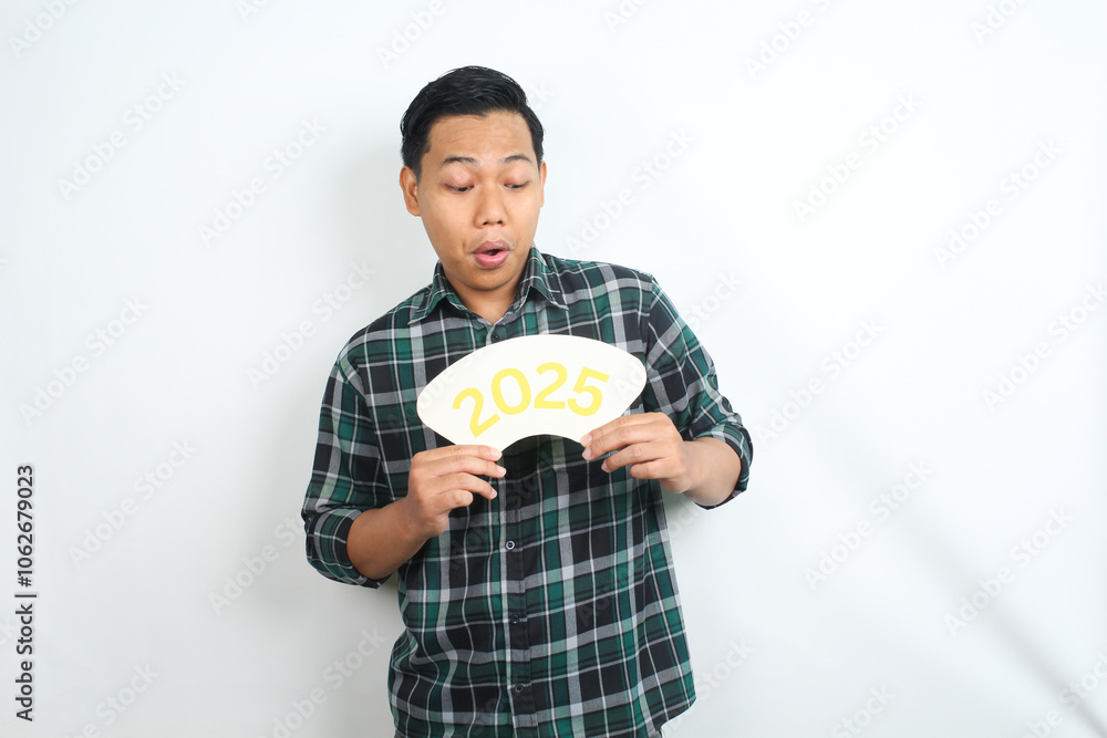 surprised asian man holding 2025 new years eve sign board and looking down isolated on white background surprised asian man holding 2025 new years eve sign board and looking down isolated on white background
