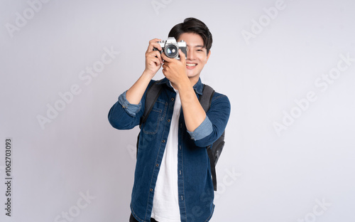 Portrait of young Asian man holding travel camera and posing on white background