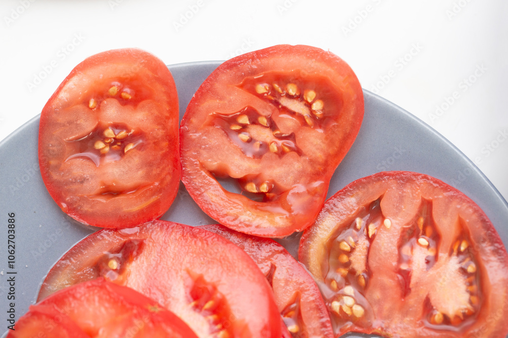 Sliced tomatoes on a plate for salad preparation. Freshly cut juicy red tomatoes, isolated on a white background. Colorful vegetable side dish or salad ingredient. Sliced tomatoes on a plate for salad preparation. Freshly cut juicy red tomatoes, isolated on a white background. Colorful vegetable side dish or salad ingredient.