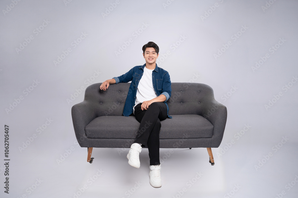 Full body image of young Asian man posing on sofa on white background Full body image of young Asian man posing on sofa on white background